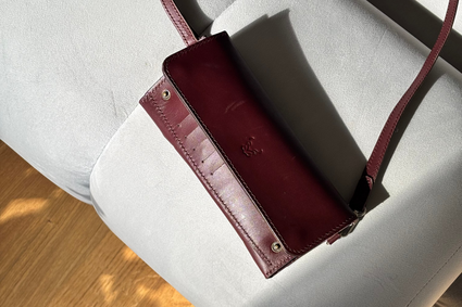 Markore Gul Sahar Maroon leather wallet on a white chair with a person's feet in sandals visible.