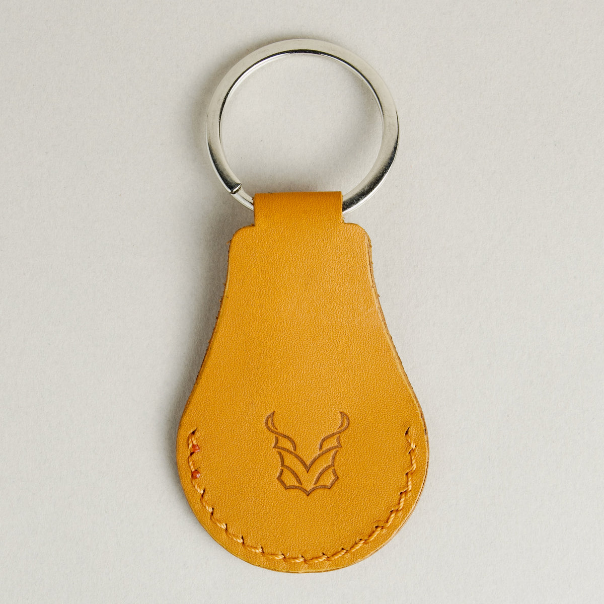 Back view of amber AirTag keychain in full-grain leather with round metal key ring and embossed logo. Markore Tag Mate.