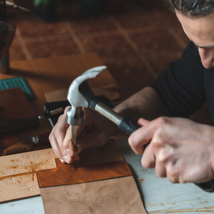 Artisan crafting a leather bag using leather tools on a wooden surface
