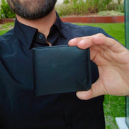 Man holding a black markore assam silk wallet made with premium full grain leather outdoors with greenery in the background