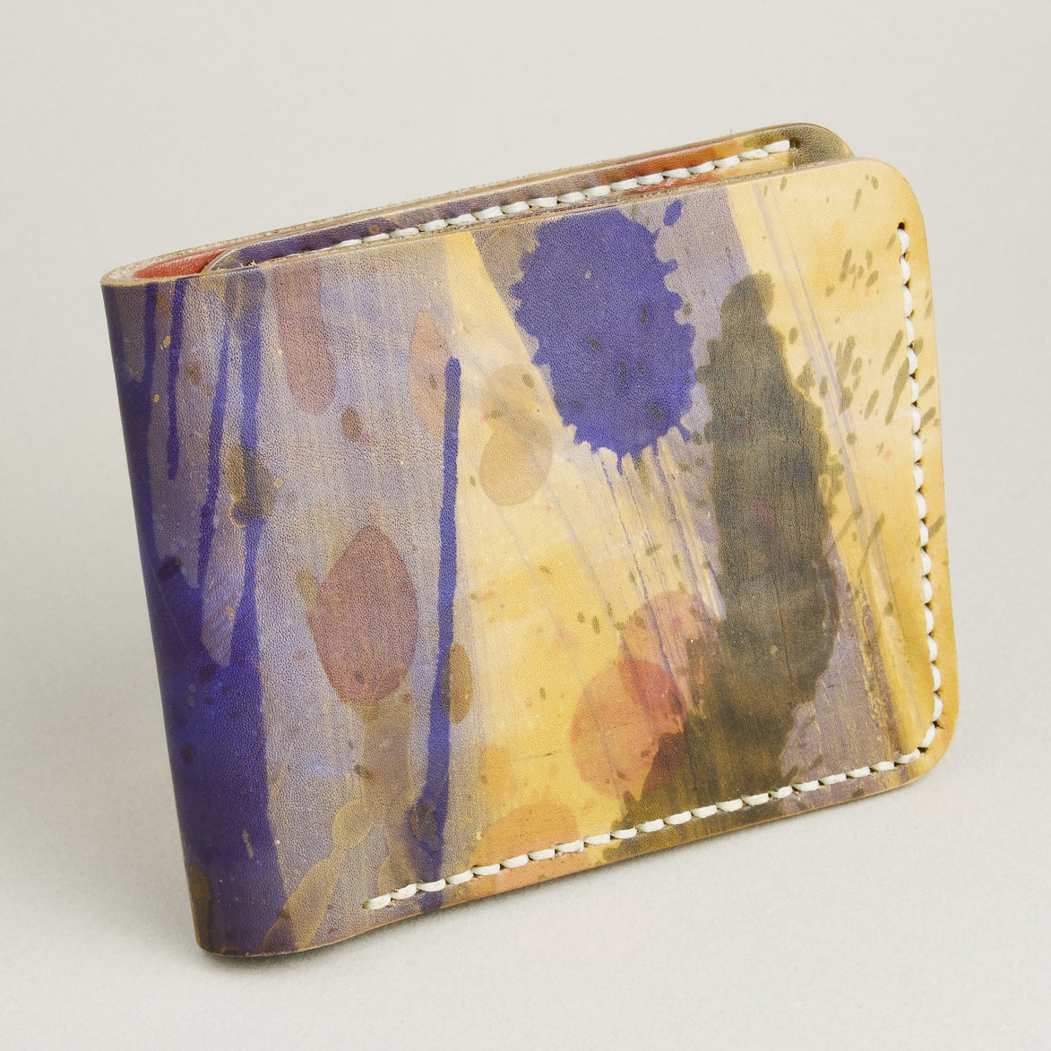 Side view of hand-painted full-grain leather bifold wallet in purple, amber, and brown, featuring handmade stitching. Markore Canvas Chaos.