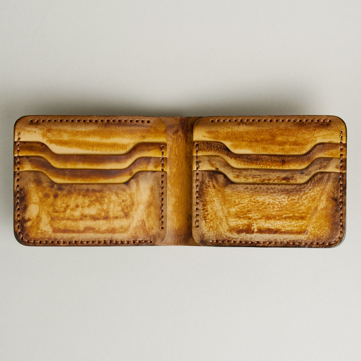 Inside view of hand-painted full-grain leather bifold wallet in amber and brown, featuring card slots and handmade stitching. Markore Canvas Flame.