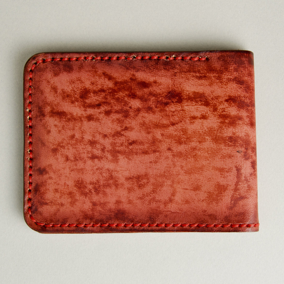 Backside view of hand-painted full-grain leather bifold wallet in red, featuring handmade stitching. Markore Canvas Flame.