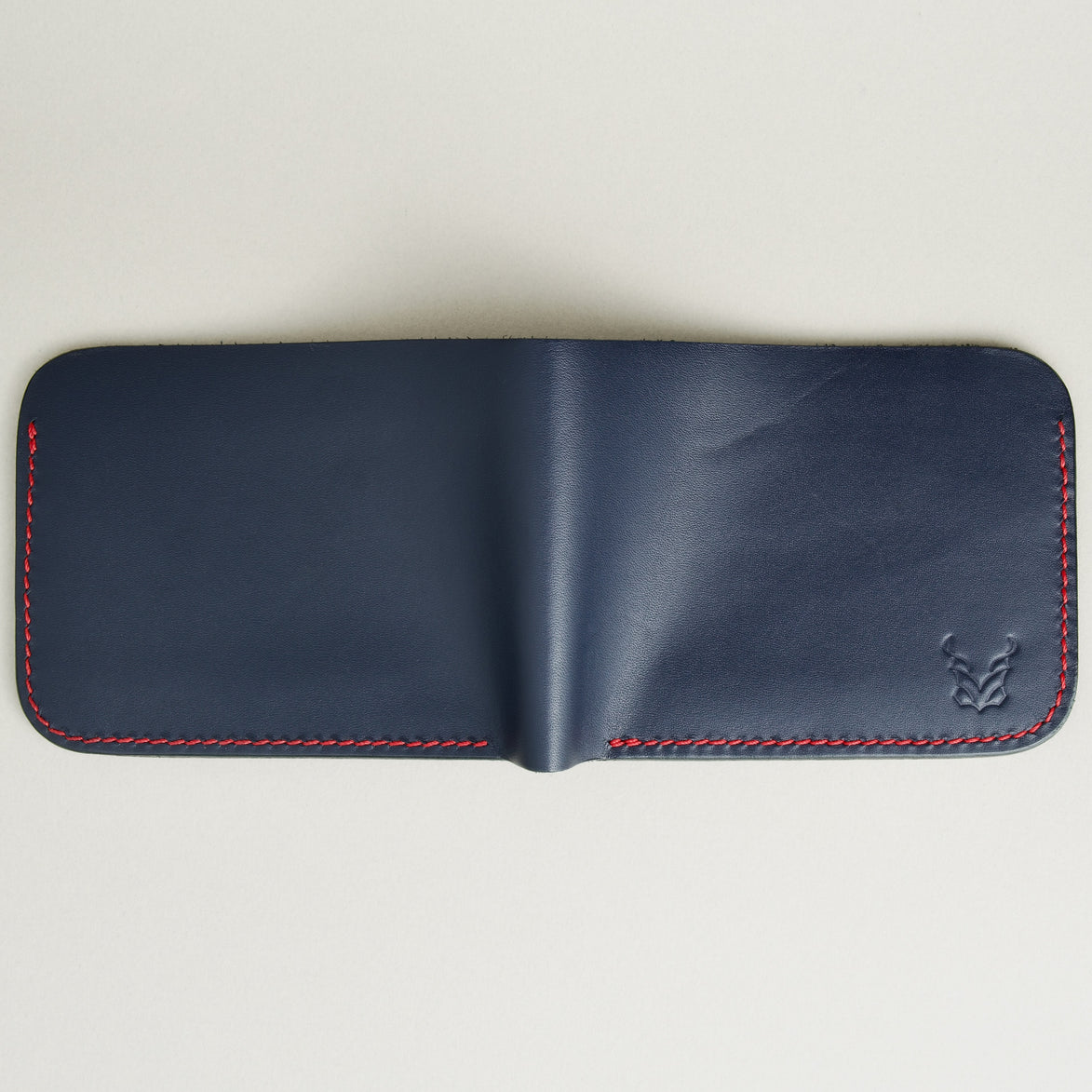 unfolded outside view of full-grain leather bifold wallet with hand-stitched red thread in Dark Blue and embossed logo. Markore Hunza Arc.