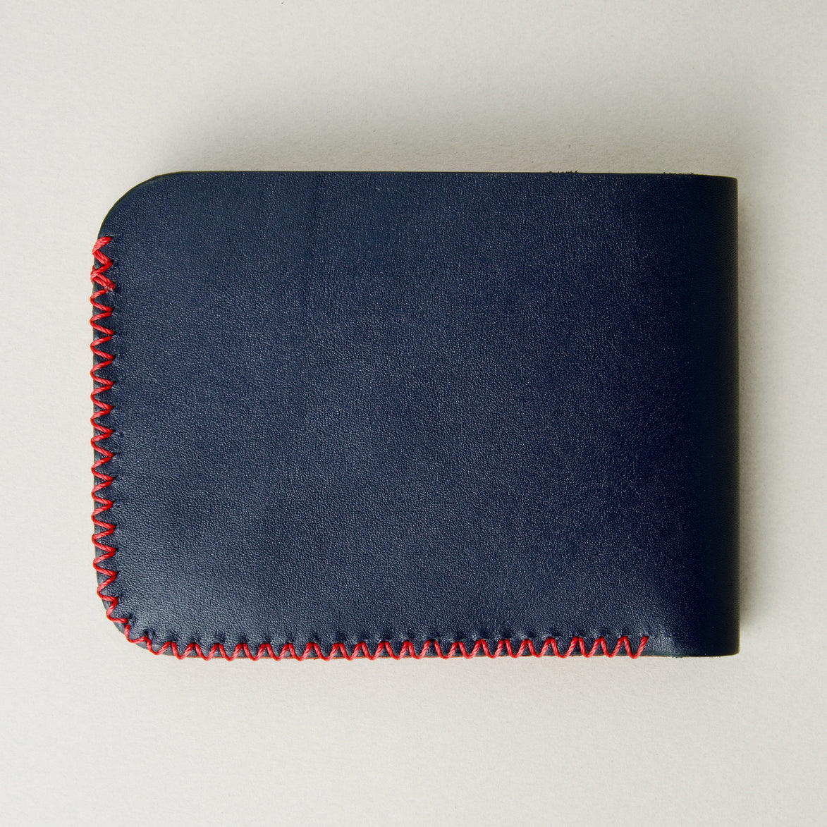 Back view of dark blue full-grain leather bifold wallet featuring red handmade cross-stitched detailing on the edges. Markore Hunza Edge.
