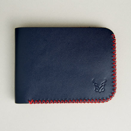 Front view of dark blue full-grain leather bifold wallet featuring handmade red cross-stitched detailing on the edges and embossed logo. Markore Hunza Edge.