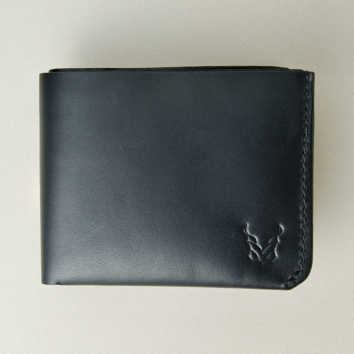 Outside view of midnight black full-grain leather wallet featuring a seamless bottom edge, handmade stitching and embossed logo. Markore Assam Silk.