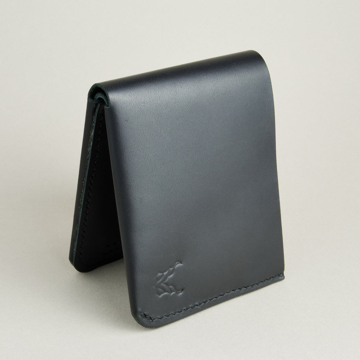 Side view of midnight black full-grain leather wallet featuring a seamless bottom edge, handmade stitching and embossed logo. Markore Assam Silk.