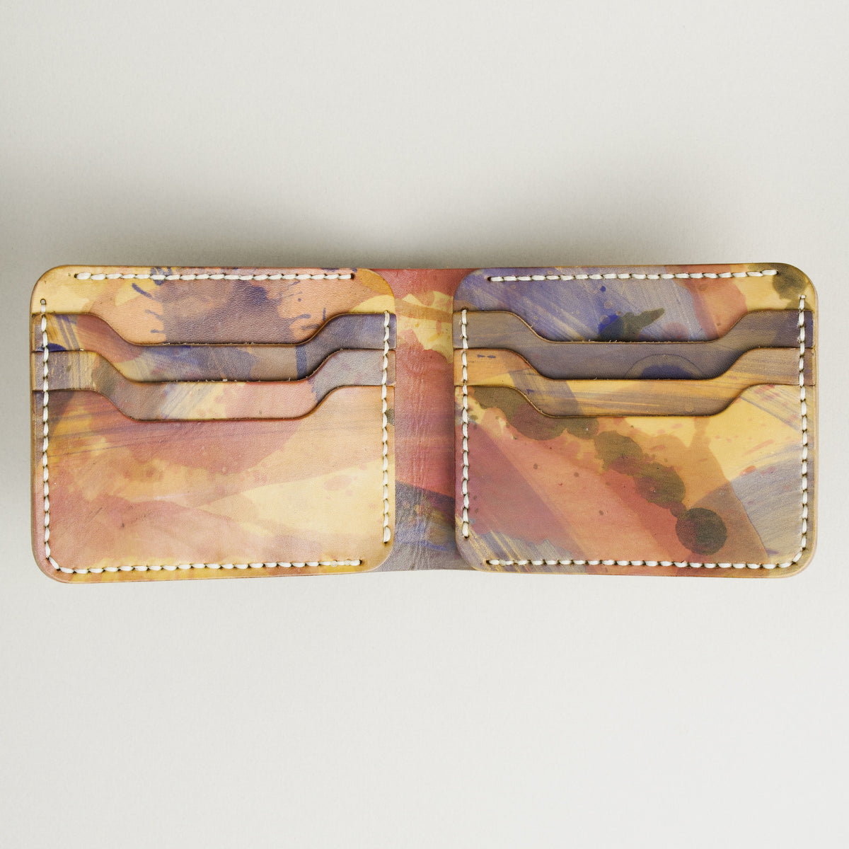 Unfolded inside view of hand-painted full-grain bifold leather wallet in purple, amber, and brown, featuring handmade stitching. Markore Canvas Chaos.