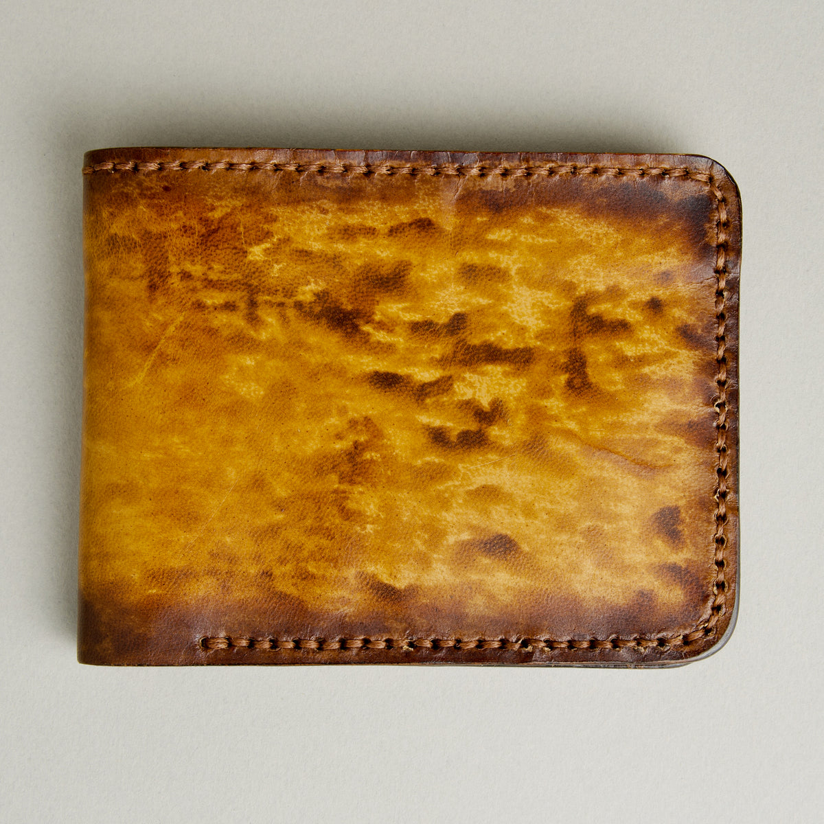 Front view of hand-painted full-grain leather bifold wallet in amber and brown, featuring handmade stitching. Markore Canvas Flame.