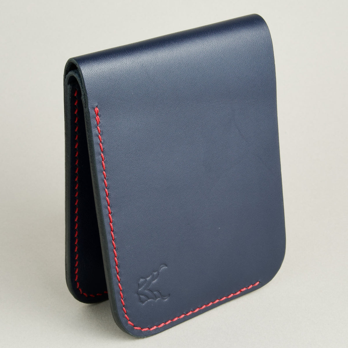 Side view of full-grain leather bifold wallet with hand-stitched red thread in Dark Blue and embossed logo. Markore Hunza Arc.