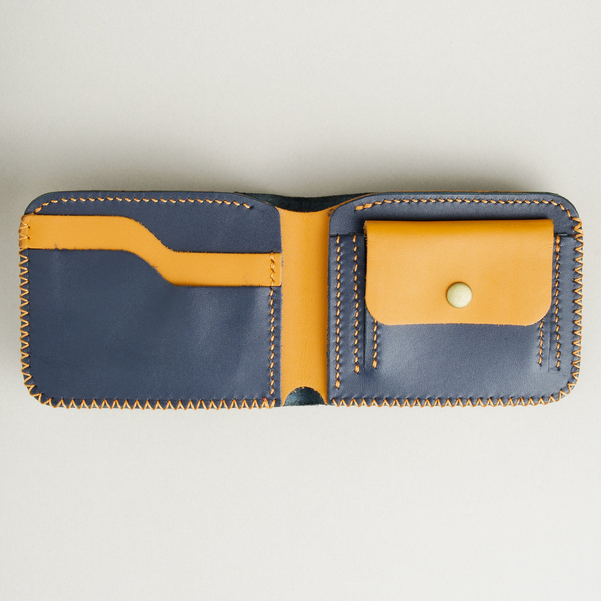 Open view of Dark Blue and amber full-grain leather bifold wallet featuring card slots, coin pocket with brass press stud, and hand-stitched detailing. Markore Hunza Edge.
