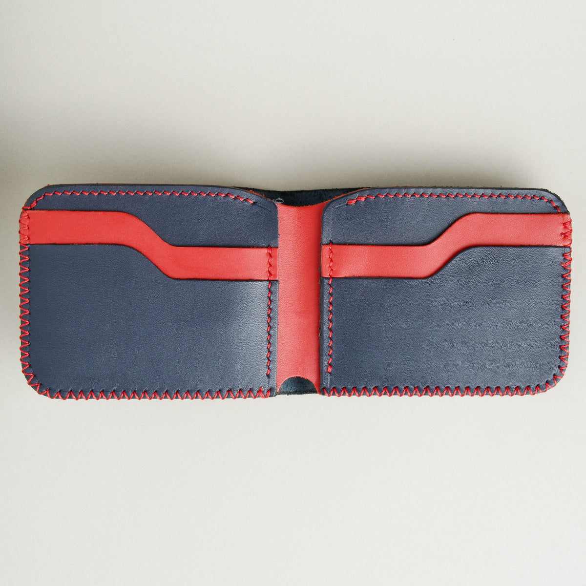 Open view of Dark Blue and Red full-grain leather bifold wallet featuring card slots and red hand-stitched detailing. Markore Hunza Edge.