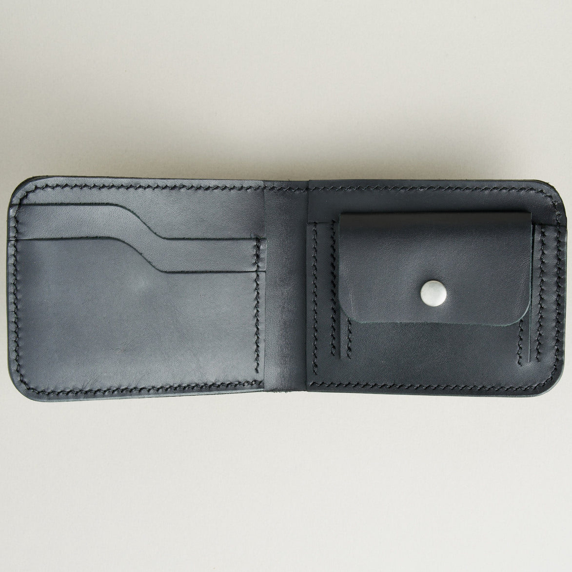 Inside view of full grain leather bifold wallet in midnight black featuring handmade stitching, a coin pocket with a stainless steel press button and card slots. Markore Hunza Fold.