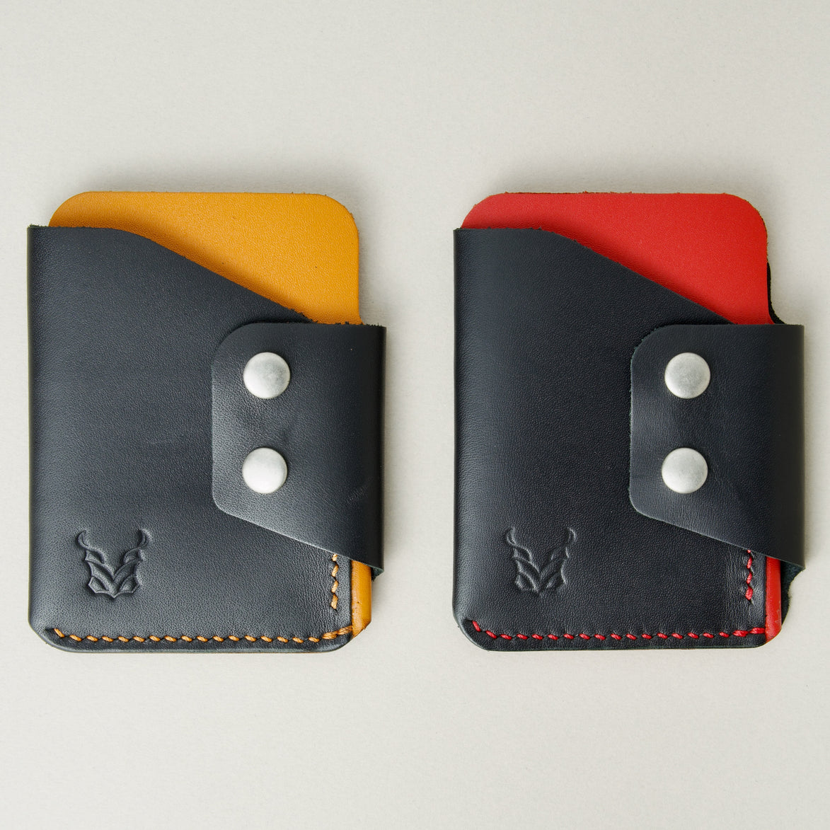 Two full grain leather card holders in black with amber and red, featuring side flap with two stainless steel press buttons, handmade stitching and embossed logo. Markore Niva Glide.