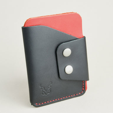 Side view of full grain leather card holder in black and red, featuring side flap with two stainless steel press buttons, red handmade stitching and embossed logo. Markore Niva Glide.
