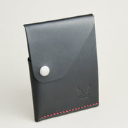 Side view of full grain leather card in midnight black with red handmade stitching, featuring a flap with stainless steel press button and embossed logo. Markore Niva Heritage.