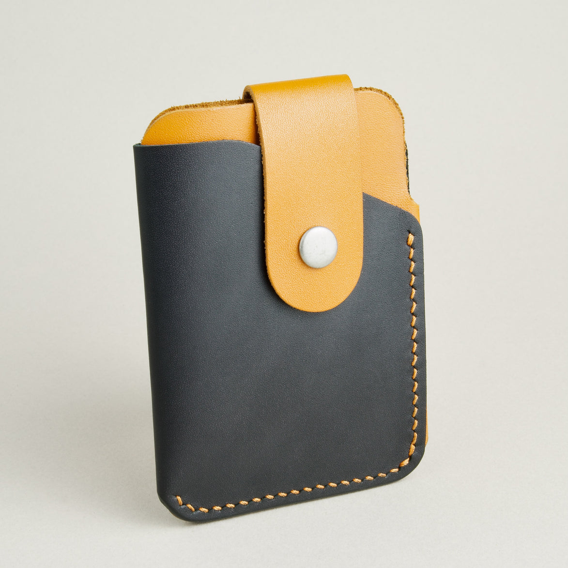 Side view of full grain leather card holder in midnight black and amber, featuring a leather loop with stainless steel press button and handmade stitching. Markore Niva Loop.