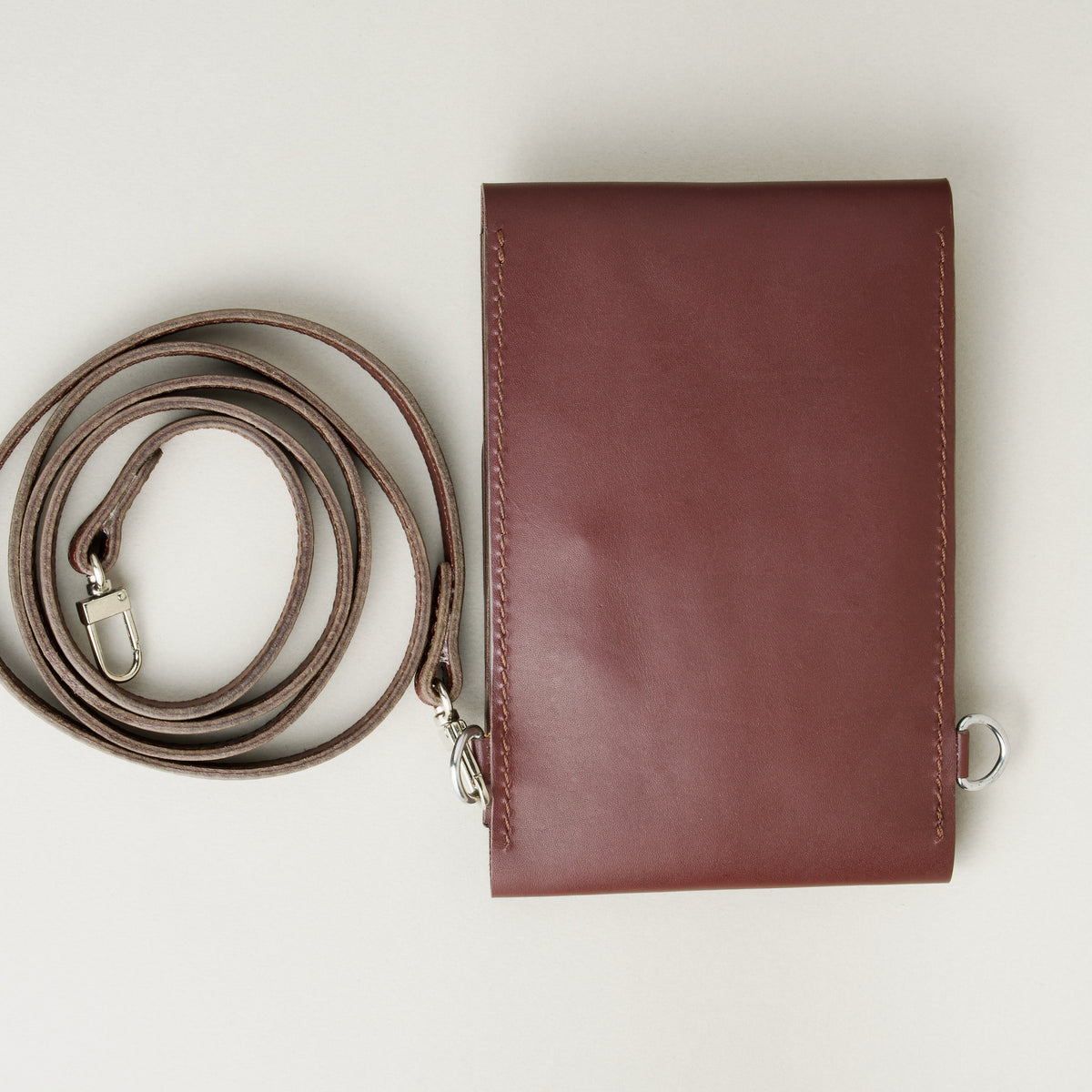 Backside view of vertical full-grain leather crossbody bag and matching shoulder strap in Espresso Brown, showing handmade stitching. Markore Nora Veldt.