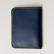 Back view of dark blue full-grain leather wallet highlighting amber handmade cross stitch detailing along the edge. Markore Ravi Edge.