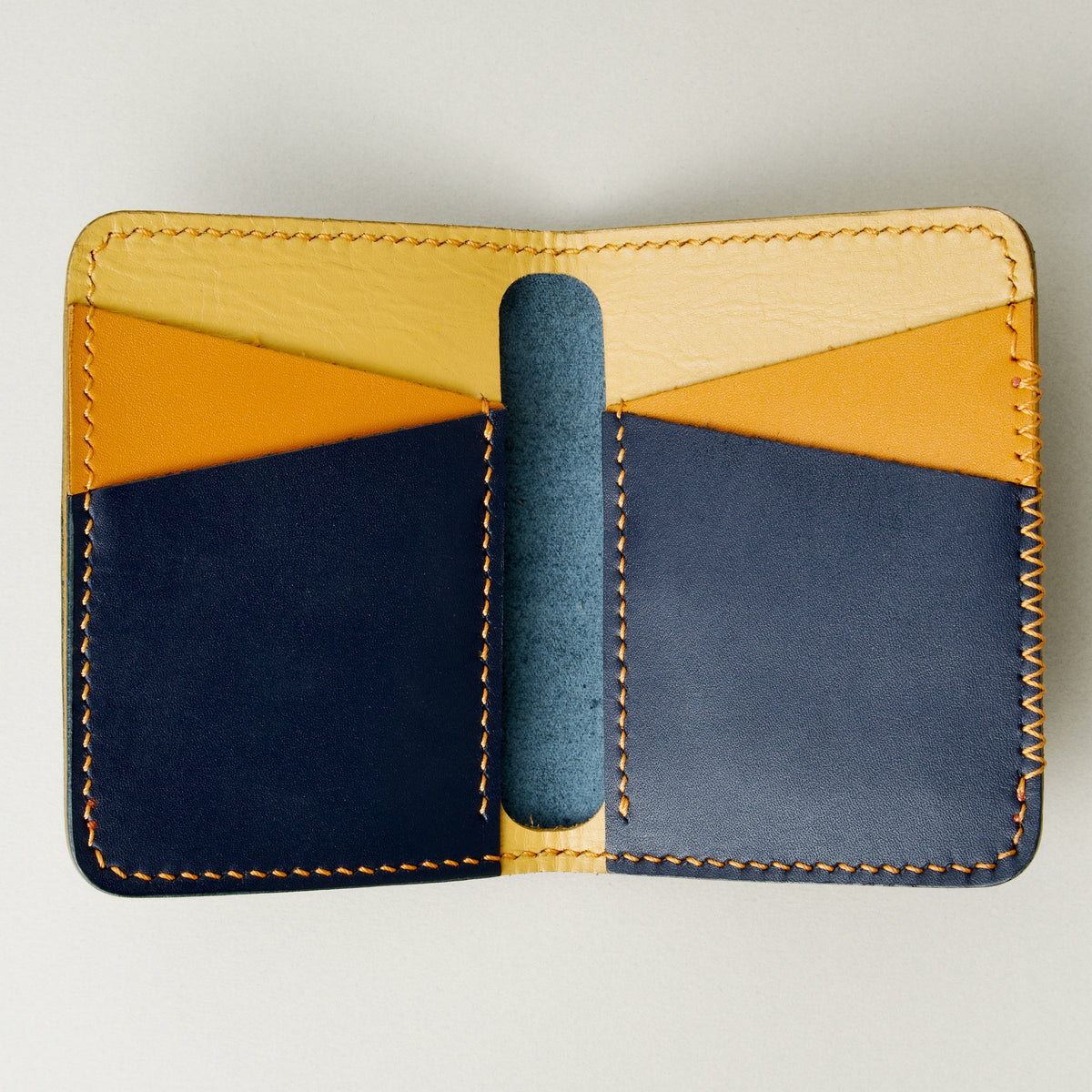 Inside view of dark blue full-grain leather wallet revealing tri-tone interior pockets in tan, amber and dark blue, card slots and handmade stitching. Markore Ravi Edge.