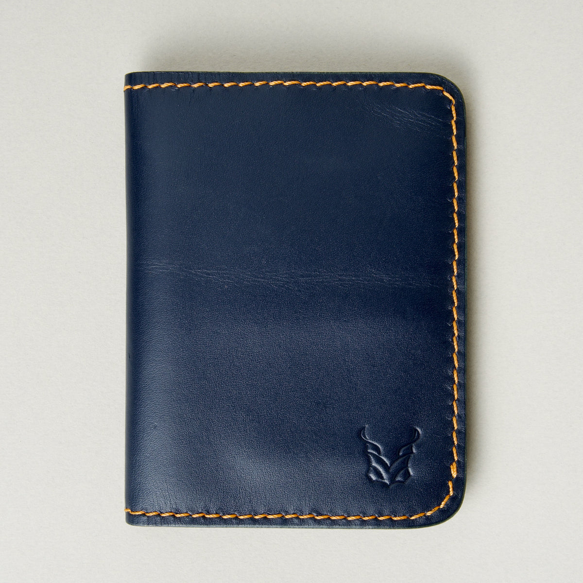 Front view of dark blue full-grain leather wallet featuring amber handmade stitching and embossed logo. Markore Ravi Edge.