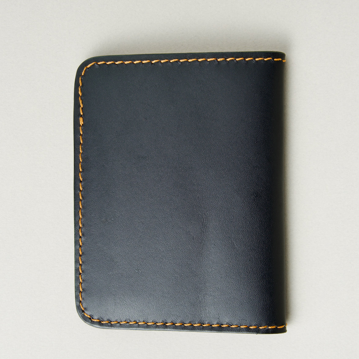 Back view of midnight black full-grain leather wallet featuring amber handmade stitching. Markore Ravi Fold.