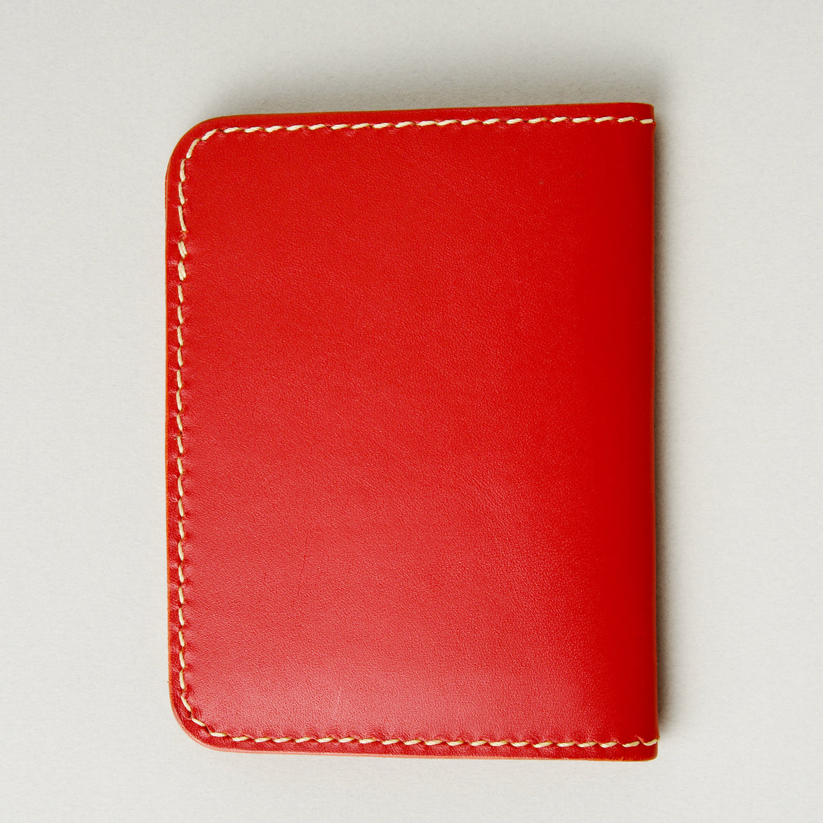 Back view of red full-grain leather wallet featuring ivory handmade stitching. Markore Ravi Fold.