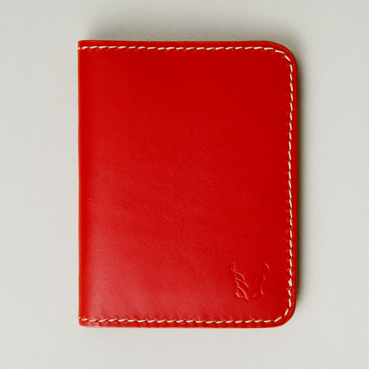 Front view of red full-grain leather wallet featuring ivory handmade stitching and embossed logo. Markore Ravi Fold.