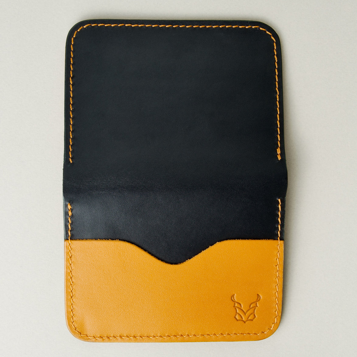 Vertical outside view of midnight black full-grain leather wallet featuring amber card slot, amber handmade stitching and embossed logo. Markore Ravi Slip.