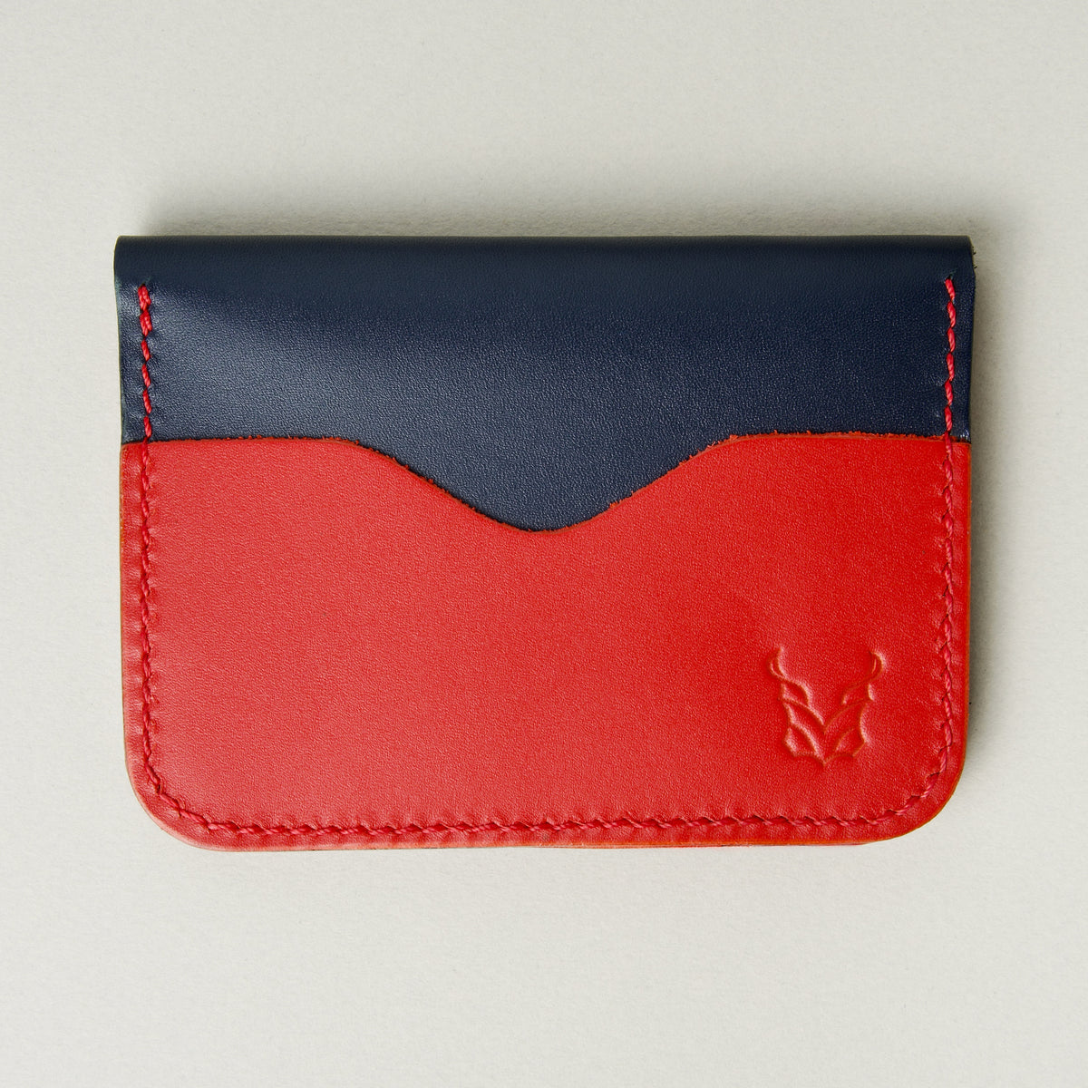 Front view of dark blue full-grain leather wallet featuring red card slot, red handmade stitching and embossed logo. Markore Ravi Slip.