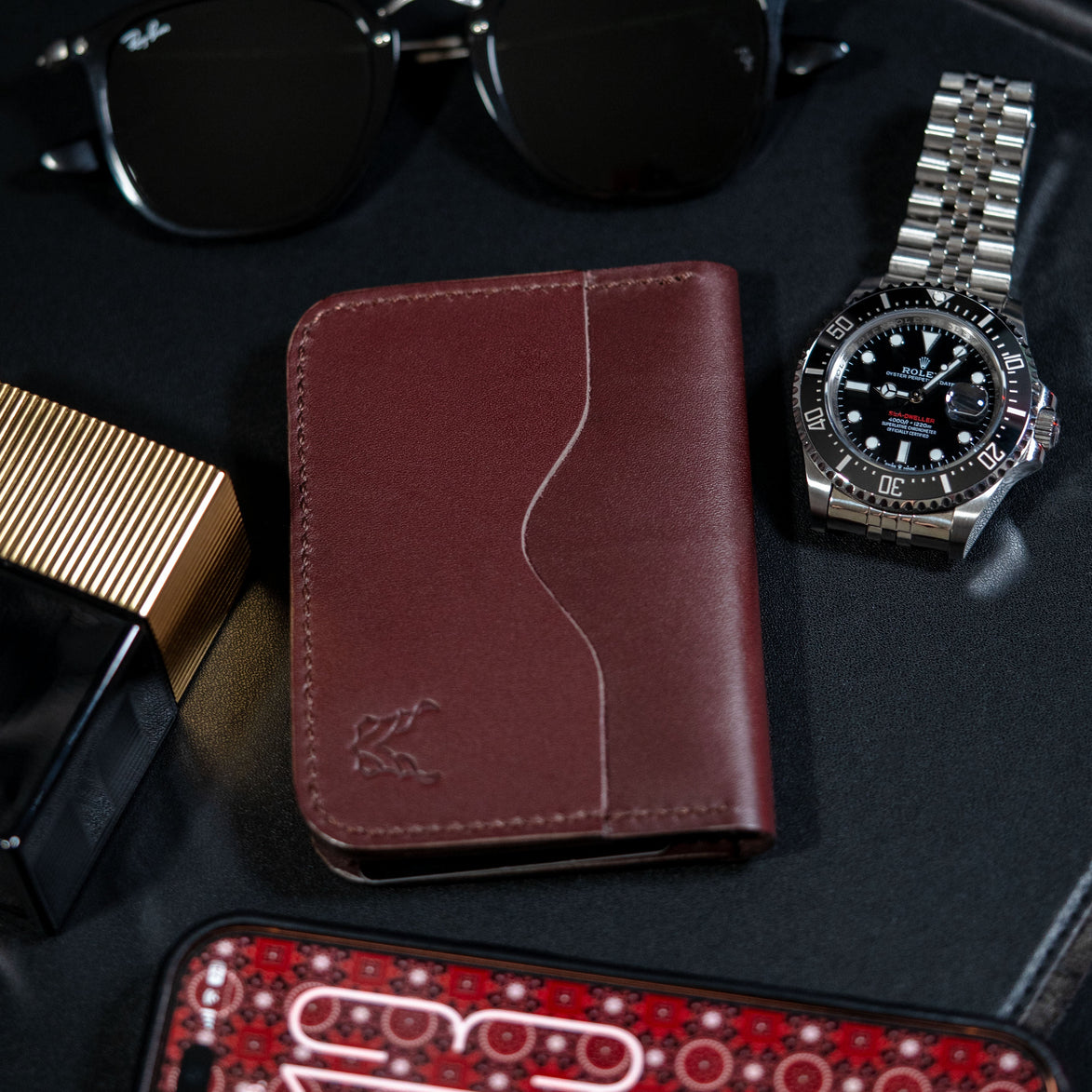 markore ravi slip slim bifold wallet in espresso brown sitting on a black table with rolex watch and phone with ajrak pattern wallpaper
