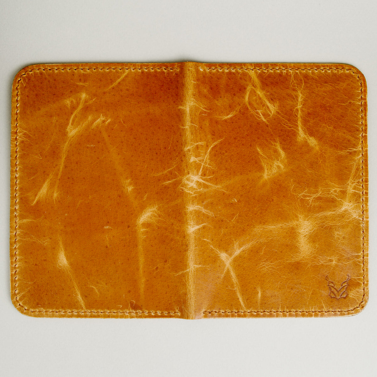 Unfolded outside view of vertical full-grain leather passport holder in amber, featuring handmade stitching and embossed logo. Markore Voyage Pass.