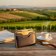 markore niva zoj leather wallet in indigo blue color with gold accents on a wooden table with a scenic background in Tuscany Italy