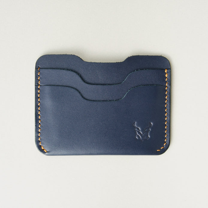 Front view of dark blue full-grain leather card sleeve featuring card slots, amber handmade stitching and embossed logo. Markore Niva Zoj.