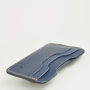 Side view of dark blue full-grain leather card sleeve featuring card slots, amber handmade stitching and embossed logo. Markore Niva Zoj.