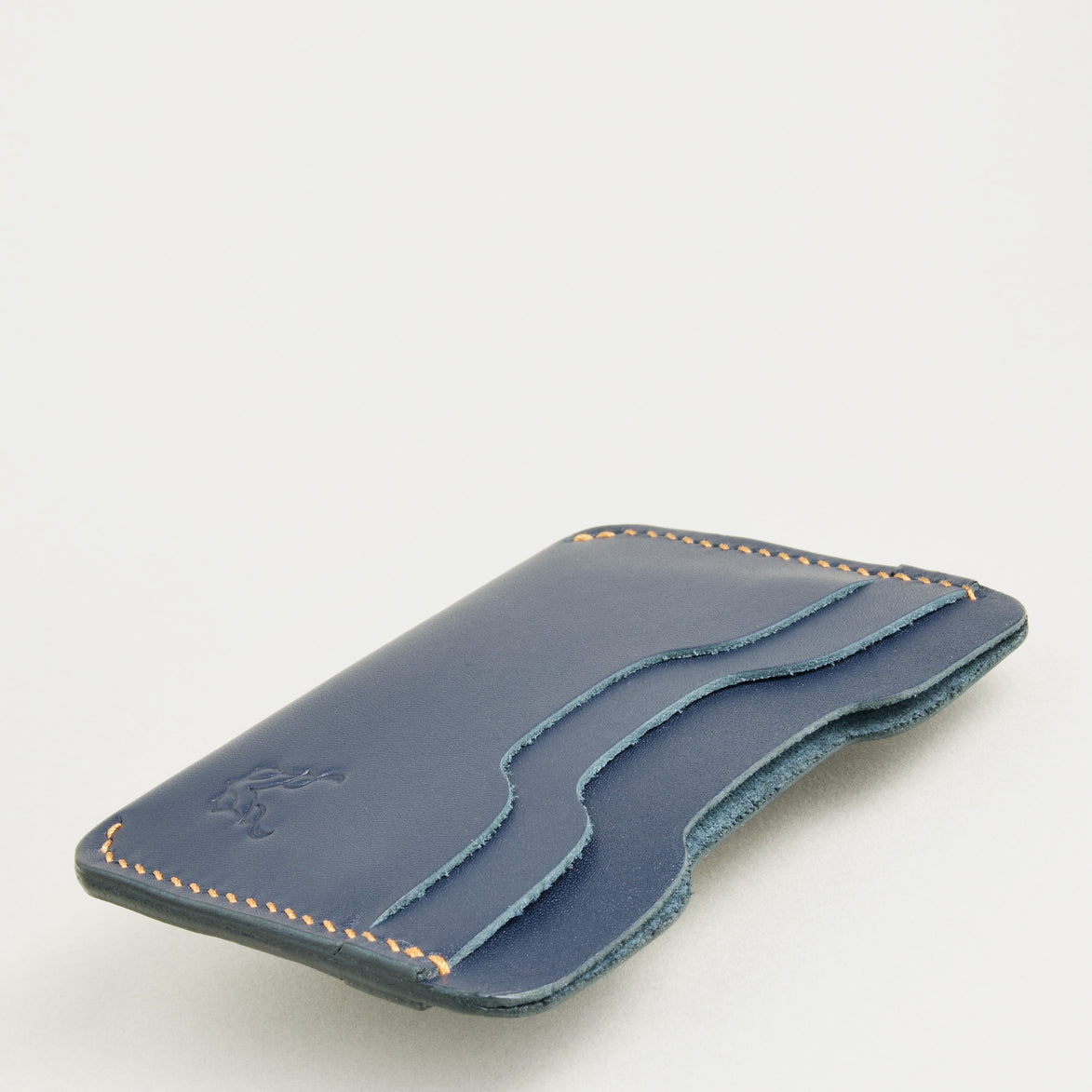 Side view of dark blue full-grain leather card sleeve featuring card slots, amber handmade stitching and embossed logo. Markore Niva Zoj.