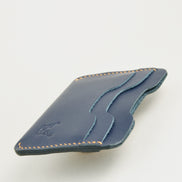 Side view of dark blue full-grain leather card sleeve featuring card slots, amber handmade stitching and embossed logo. Markore Niva Zoj.